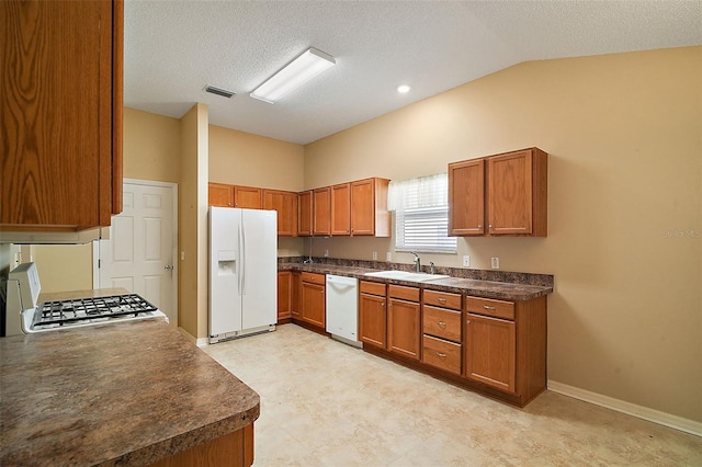 kitchen featuring visible vents, brown cabinets, a sink, dark countertops, and white appliances