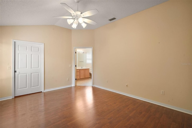 unfurnished bedroom featuring visible vents, a textured ceiling, wood finished floors, baseboards, and vaulted ceiling