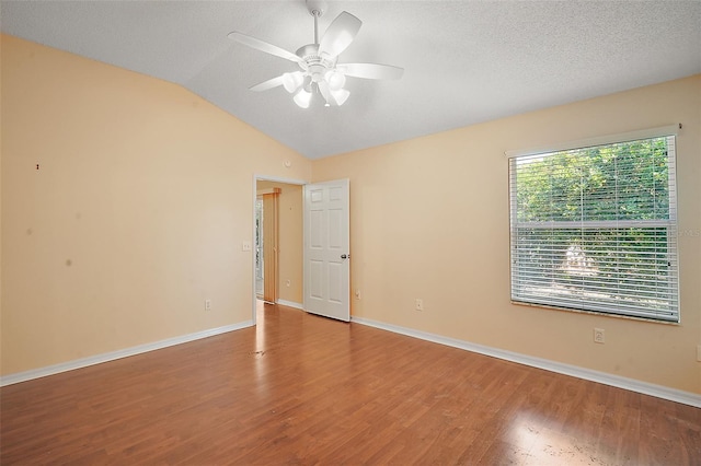 empty room featuring a textured ceiling, wood finished floors, baseboards, ceiling fan, and vaulted ceiling