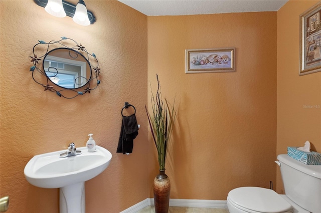 half bathroom with toilet, a textured wall, and baseboards