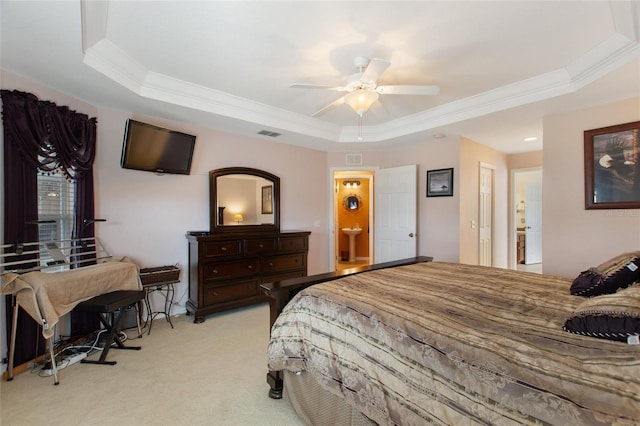 bedroom with a tray ceiling, crown molding, light colored carpet, and ensuite bathroom