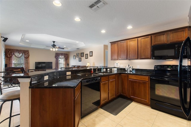 kitchen featuring visible vents, black appliances, a raised ceiling, a kitchen breakfast bar, and open floor plan