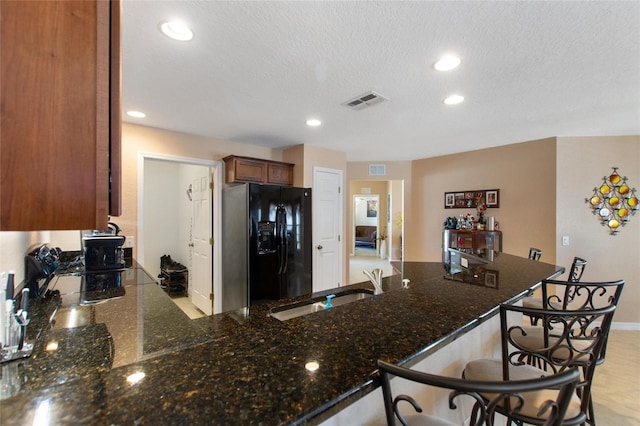 kitchen with dark stone countertops, visible vents, a peninsula, a sink, and black fridge