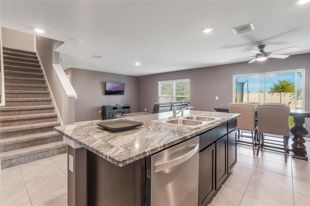 kitchen featuring light stone countertops, a center island with sink, visible vents, a sink, and stainless steel dishwasher