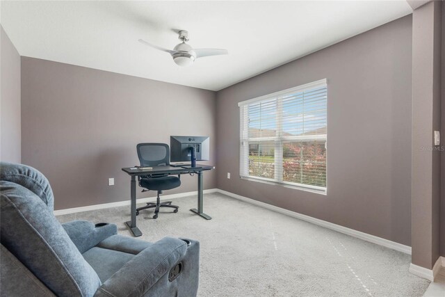 carpeted office space featuring a ceiling fan and baseboards