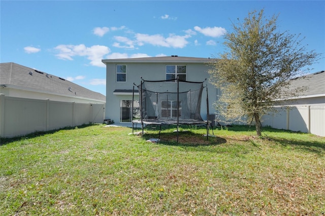 back of property featuring a yard, a fenced backyard, stucco siding, and a trampoline