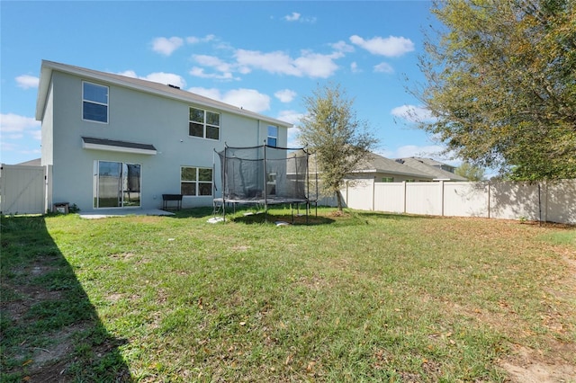 back of house featuring a trampoline, a lawn, fence, and stucco siding
