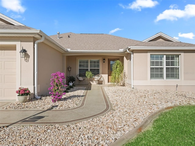 doorway to property featuring a shingled roof, a garage, and stucco siding