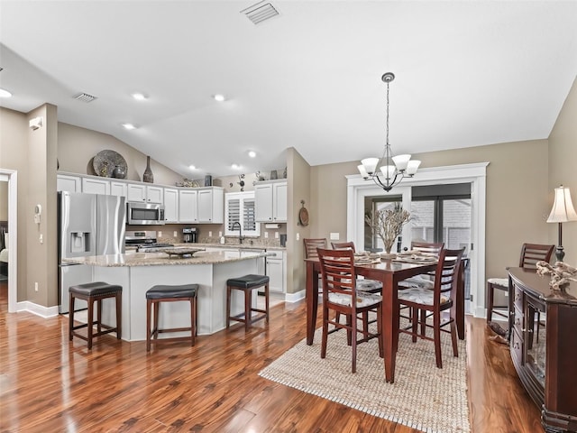 dining space with a chandelier, visible vents, wood finished floors, and vaulted ceiling