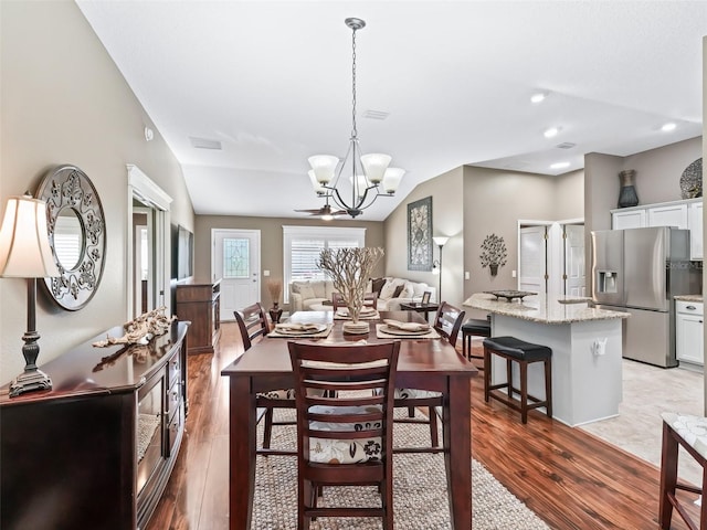 dining room with vaulted ceiling, a notable chandelier, light wood-style floors, and visible vents