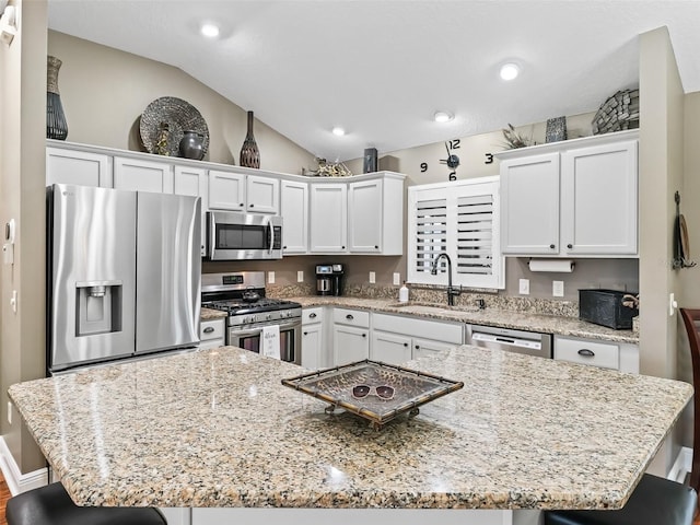 kitchen with a kitchen bar, vaulted ceiling, white cabinets, stainless steel appliances, and a sink