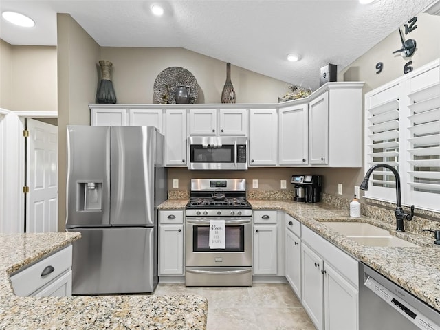 kitchen with appliances with stainless steel finishes, white cabinetry, lofted ceiling, and a sink