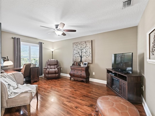 living area with visible vents, a ceiling fan, a textured ceiling, wood finished floors, and baseboards