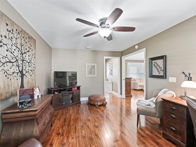 living room featuring wood finished floors, visible vents, baseboards, ceiling fan, and a textured ceiling