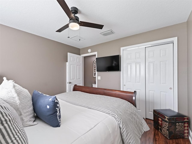 bedroom with wood finished floors, visible vents, ceiling fan, a closet, and a textured ceiling