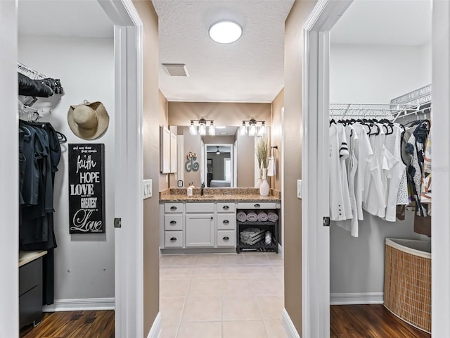 bathroom featuring a walk in closet, vanity, baseboards, and a textured ceiling