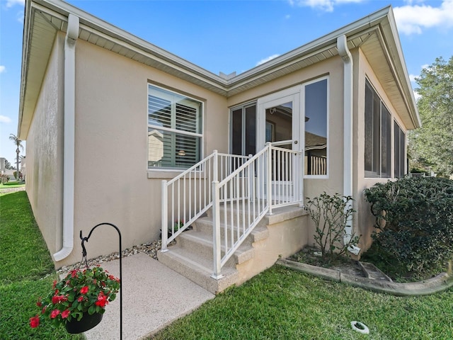 view of exterior entry with stucco siding and a yard