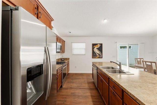 kitchen featuring brown cabinetry, dark wood-style flooring, stainless steel appliances, and a sink