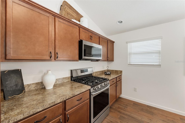 kitchen featuring brown cabinets, dark wood-type flooring, lofted ceiling, appliances with stainless steel finishes, and baseboards