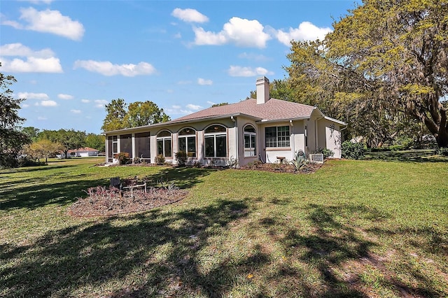 back of house featuring stucco siding, a chimney, a lawn, and a sunroom