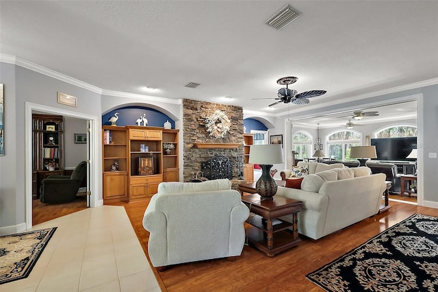 living area featuring visible vents, ornamental molding, a ceiling fan, wood finished floors, and a fireplace