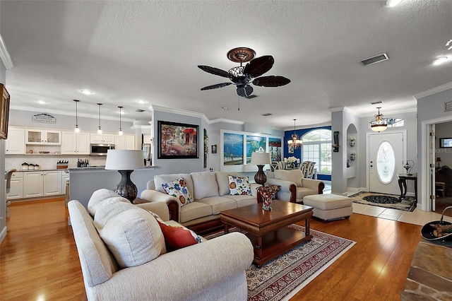 living area with light wood-type flooring, visible vents, ceiling fan with notable chandelier, a textured ceiling, and crown molding