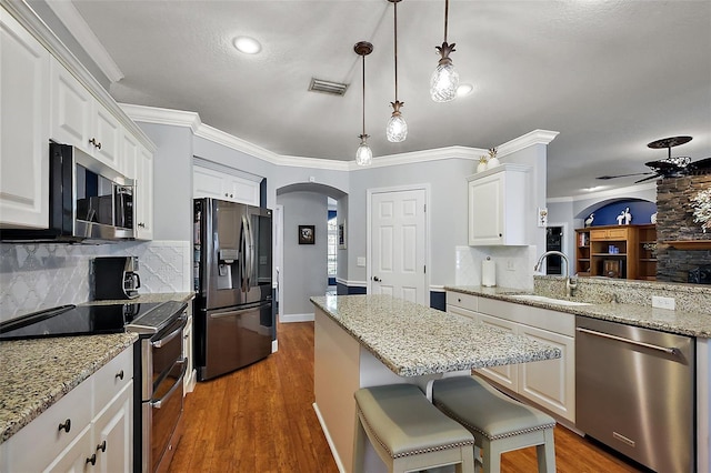 kitchen featuring ornamental molding, arched walkways, stainless steel appliances, a ceiling fan, and a sink