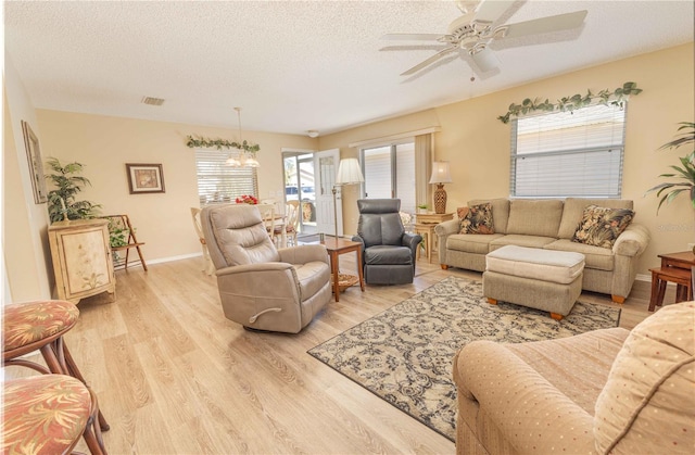 living room with light wood-type flooring, visible vents, ceiling fan with notable chandelier, a textured ceiling, and baseboards