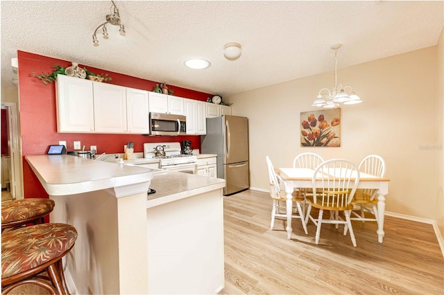 kitchen featuring light wood finished floors, a breakfast bar, light countertops, appliances with stainless steel finishes, and white cabinetry