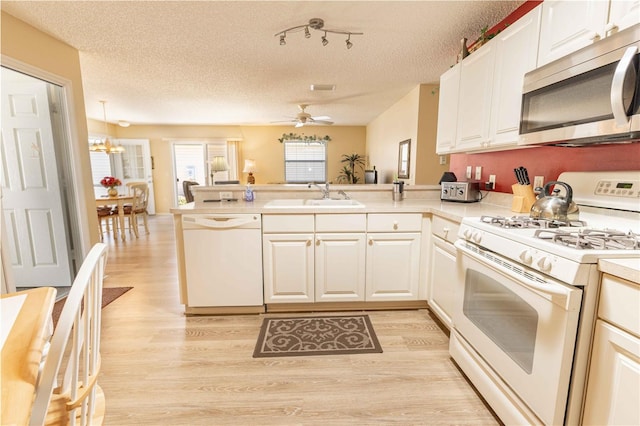 kitchen with white appliances, light wood finished floors, a peninsula, a sink, and light countertops