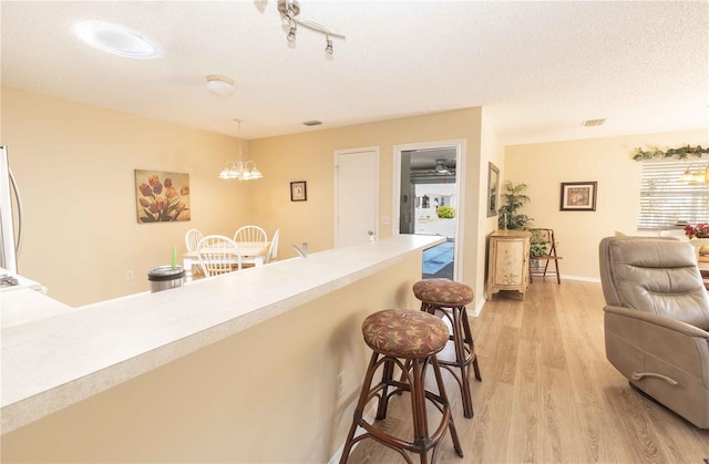 kitchen with light wood-type flooring, a notable chandelier, a kitchen breakfast bar, a textured ceiling, and hanging light fixtures