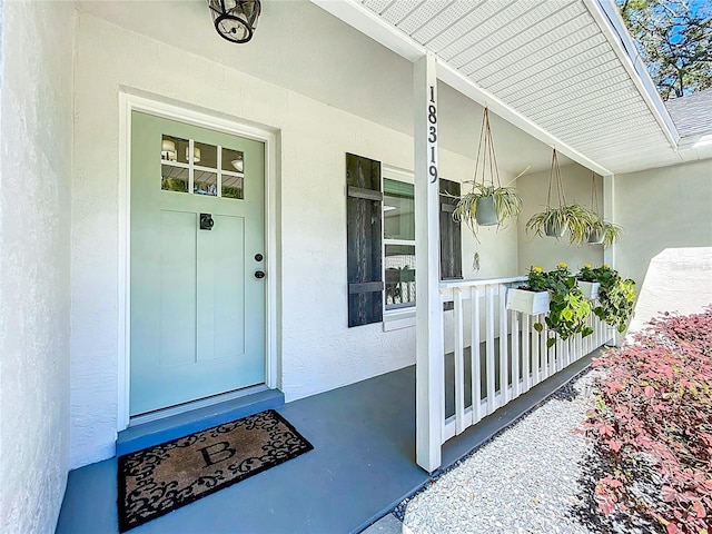 property entrance with covered porch and stucco siding