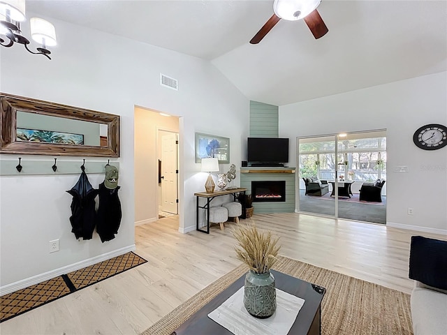 living area featuring visible vents, light wood-type flooring, ceiling fan with notable chandelier, a warm lit fireplace, and high vaulted ceiling