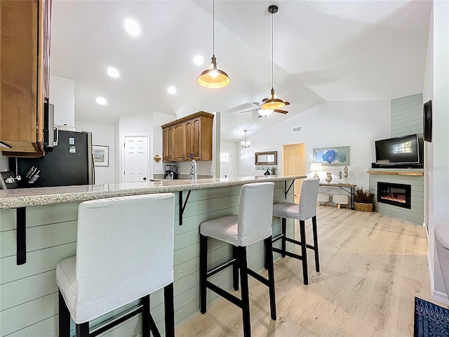 kitchen with brown cabinets, a breakfast bar, lofted ceiling, freestanding refrigerator, and light wood-type flooring