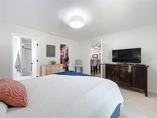 bedroom with a spacious closet, connected bathroom, light carpet, a closet, and a textured ceiling