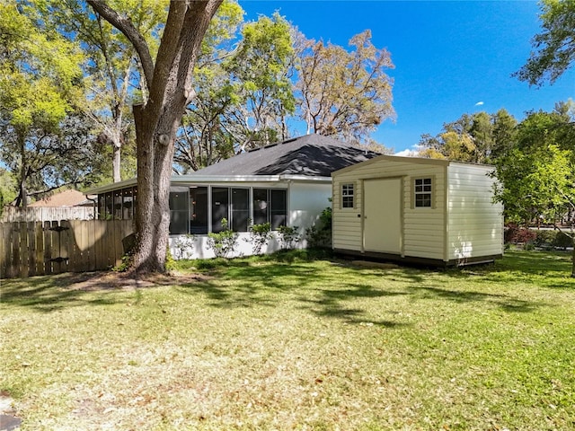 rear view of house featuring fence, a yard, a storage shed, an outdoor structure, and a sunroom