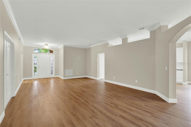 unfurnished living room featuring light wood-style flooring, arched walkways, visible vents, and ornamental molding