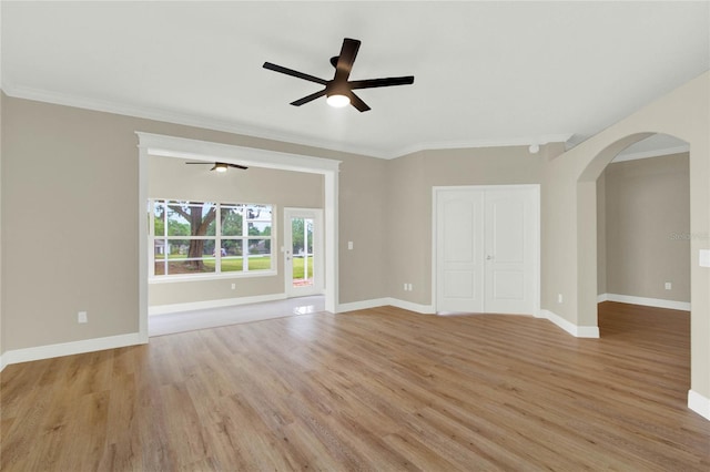 empty room with a ceiling fan, arched walkways, light wood-style floors, crown molding, and baseboards