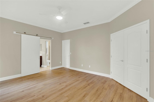 unfurnished bedroom featuring a barn door, visible vents, baseboards, and light wood-style floors