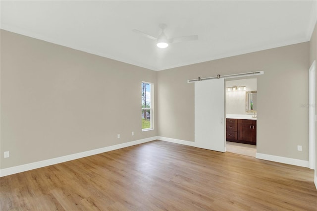 empty room with a barn door, baseboards, light wood-type flooring, and a ceiling fan