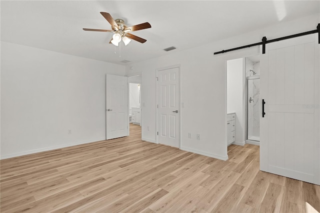 unfurnished bedroom featuring visible vents, ceiling fan, a barn door, light wood-style floors, and ensuite bath