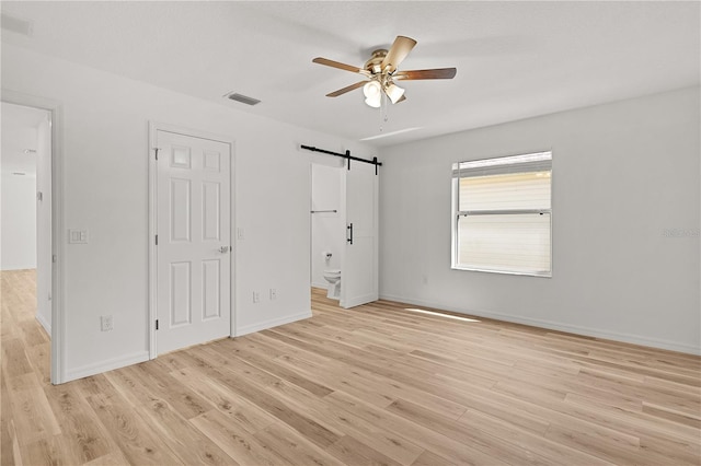 unfurnished bedroom featuring a barn door, light wood-style floors, visible vents, and baseboards