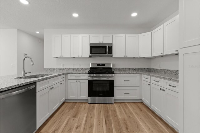 kitchen featuring recessed lighting, appliances with stainless steel finishes, light wood-style floors, white cabinets, and a sink