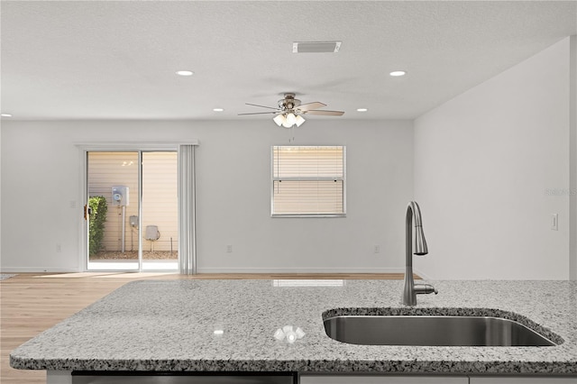 kitchen featuring light stone counters, visible vents, a ceiling fan, and a sink