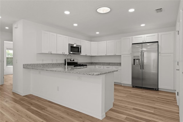 kitchen with light wood-type flooring, stainless steel appliances, a peninsula, and white cabinetry