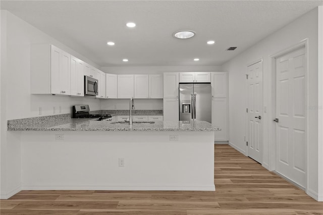 kitchen featuring visible vents, a peninsula, a sink, stainless steel appliances, and light wood-type flooring