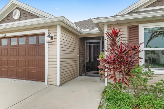 entrance to property featuring concrete driveway, an attached garage, and a shingled roof