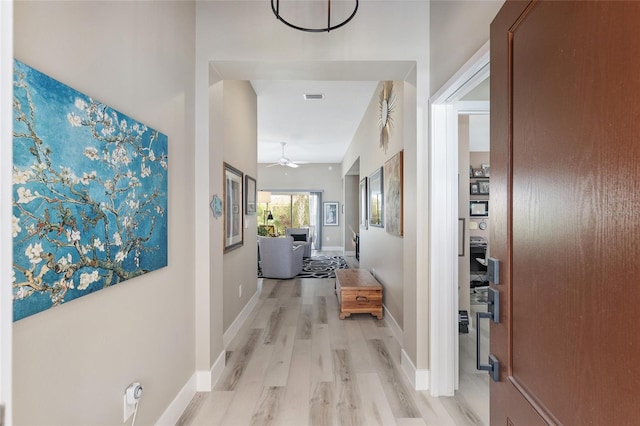 hall featuring light wood finished floors, visible vents, and baseboards