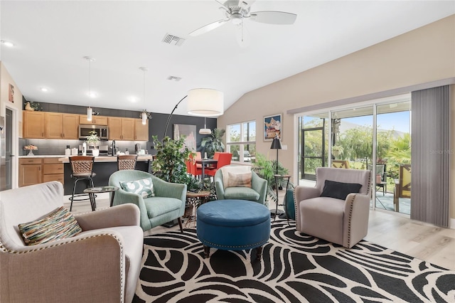 living area featuring visible vents, lofted ceiling, ceiling fan, and light wood finished floors