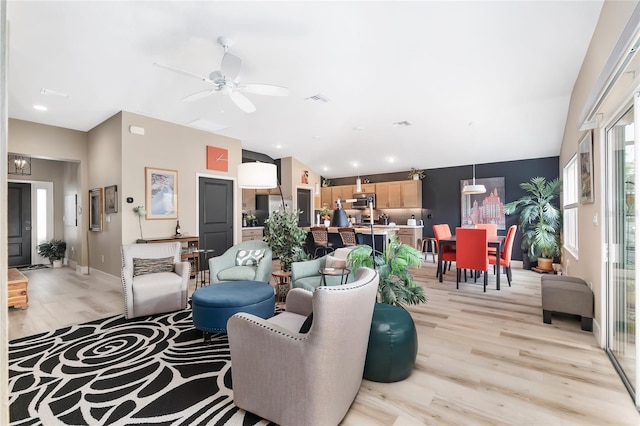 living area with baseboards, ceiling fan, vaulted ceiling, and light wood finished floors